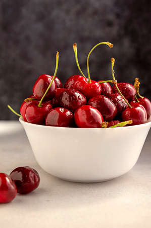 Fresh red cherries in white bowl, on dark background. Summer delicious fruits