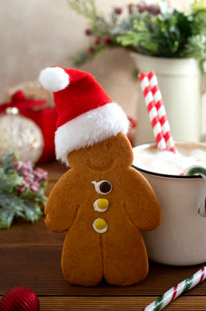 Gingerbread man cookie with Christmas red hat and hot drink on wooden background winter decorationsの写真素材