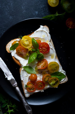 Cream cheese toast with cherry, colorful tomatoes. Black, moody background. Top viewの写真素材
