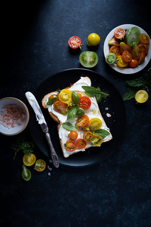 Cream cheese toast with cherry, colorful tomatoes. Black, moody background. Top viewの写真素材