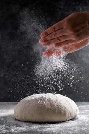 Raw dough and sprinklling flour over dark background. Cooking bread or pizza. Action, movement food photoの写真素材