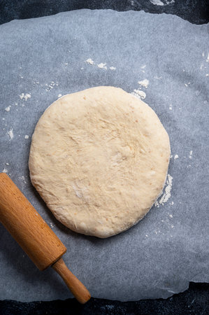 Raw sourdough, dough for homemade pizza on dark background with rolling pin, dark backgroundの写真素材