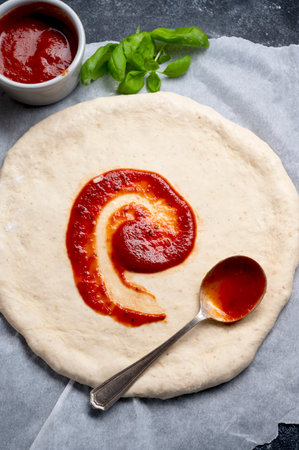 Cooking pizza, tomatoe sauce on raw dough. Homemade sourdoguh pizza dough, top viewの写真素材