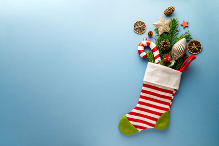Christmas greeting with christmas gift sock, candy cane, baubles, candy canes on blue background. Flat lay. Copy space for textの写真素材