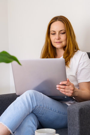 Woman working online, sitting in armchair and using laptopの写真素材