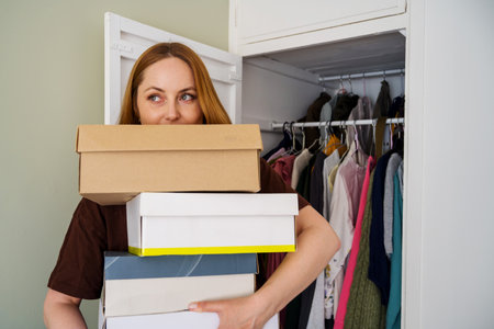 Woman holding cardboard shoes boxes next to builtin closet.の写真素材