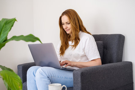 Woman working online, sitting in armchair and using laptopの写真素材