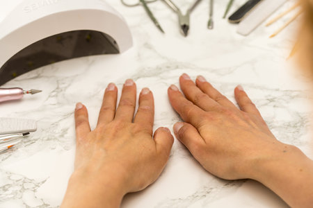 Nail manicure at home, female hands on the table with uv lamp and manicure toolsの写真素材