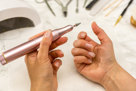 Gel nail manicure at home, female hands with nail drill bitの写真素材