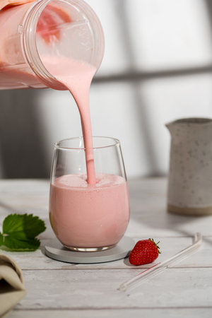 Pouring strawberry smoothie. Fruit healthy milkshake glass with fresh berries.の写真素材