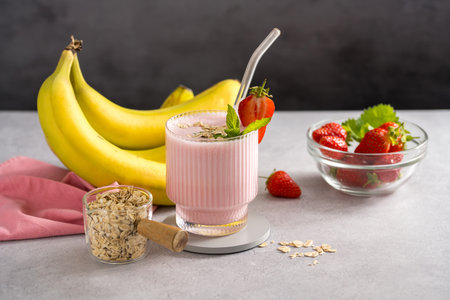 Pink strawberry, banana, oats smoothie in a glass with fresh fruits, dark backgroundの写真素材