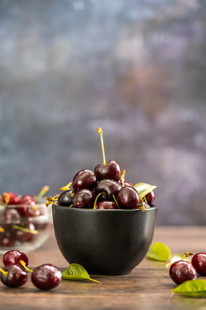 Fresh cherries fruits in a black bowl, wooden background. Summer fruits. Copy spaceの写真素材