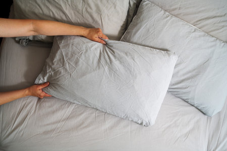 Female hands holding a pillow with fresh clean pillowcases, grey cotton bed sheets