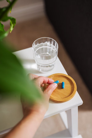 Blue capsule pills with glass of water on the table, lifestyle shot