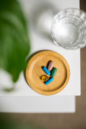Colourful capsule pills with glass of water on the table, lifestyle shot