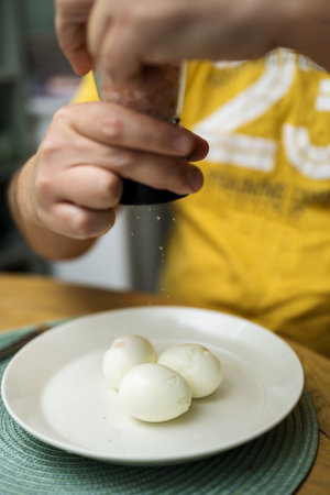 Boiled eggs for breakfast. Mans hand salting three boiled eggs in a plate. Eating proteins