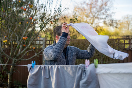 Man hangs up laundry to dry outdoors on hanging rope. Father performs home duties