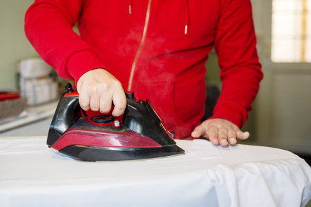 Man's hand ironing clothes on an ironing board at homeの写真素材