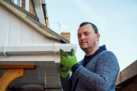 Man on a ladder cleaning fallen autumn leaves and moss from house roof gutter. Home maintenance, gutter cleaningの写真素材