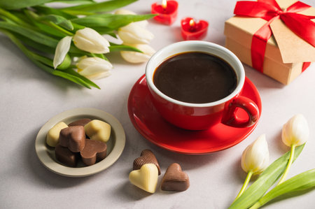 Valentines day. Cup of coffee, heart chocolates, gift box and spring white tulip flower bouquet.の写真素材