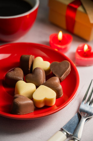 Valentines Day chocolate candies in red plate served with a cup of coffee and candlesの写真素材