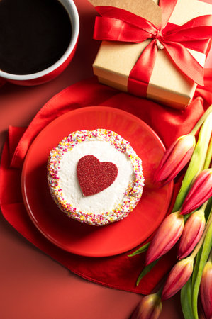 Valentines Day festive red background. Cake with red heart, cup of coffee, gift box and spring red tulip flower bouquet. Top viewの写真素材