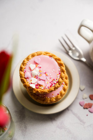 Pink mini tarts with heart shaped sprinkles, cup of coffee and bouquet of spring red tulips.の写真素材