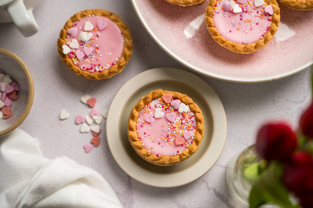 Valentine's day. Pink mini tarts with heart shaped sprinkles, cup of coffee and bouquet of spring red tulips.の写真素材