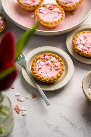 Valentine's day. Pink mini tarts with heart shaped sprinkles, cup of coffee and bouquet of spring red tulips.の写真素材
