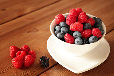 Ripe sweet different berries in white bowl on rustic wooden table. Harvest Concept