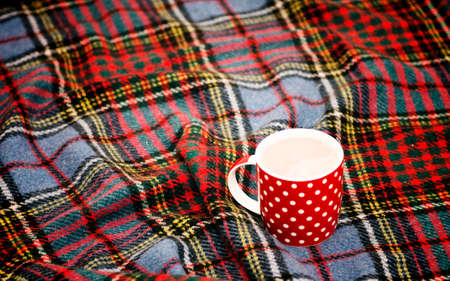 Red dotted teacup with hot chocolate on a Scottish blanket. Cozy home concept with red porcelain mug. A Cup of festive hot chocolate. Traditional homemade Christmas advertising cocoa. New year's still lifeの写真素材