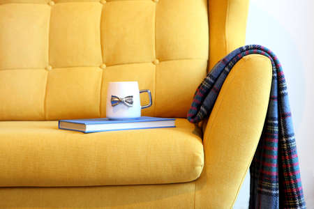 Cup of tea and blue book on yellow coach with blanket. Still life details in home interior of living room. Cozy interior, gender free interior. Modern interior in the living room.の写真素材
