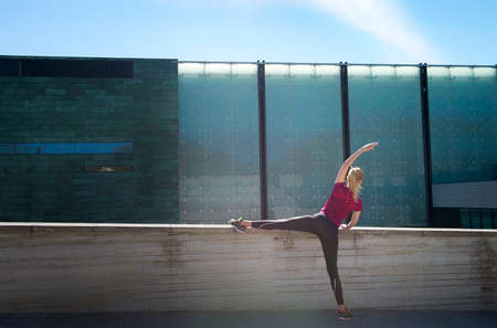Sporty young girl in top and leggings doing yoga streching exercise pose. Pretty woman holding hands and legs, strenching all body, modernoutdoor at the city. Concept of sport and health.の写真素材