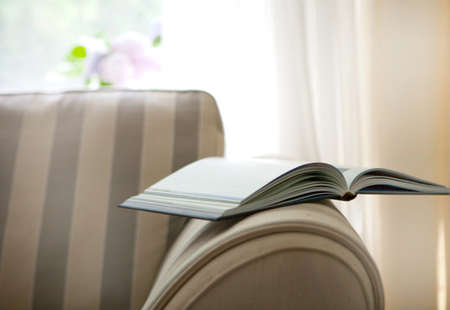 Book on the chair behind the window in a white cosy interior. vintage style with modern interior style and brown sofa or chairの写真素材