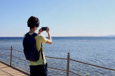 Hipster guy taking pictures of amazing landscape on mobile smart phone digital camera of a mountain...
