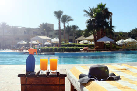 taning lotion, juices on the beach table with a blue straw hat near the swimming pool at the resort...