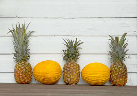 Melons and Pineapple behind the white wooden-timber background. Funny summer Wallpaper. fruit decorationsの写真素材