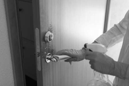 cleaning door with sanitarizer - woman's hand in blue medical protective glove with rag wiping...