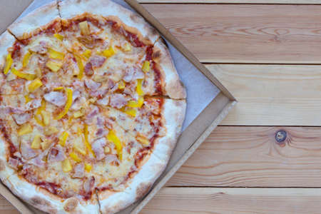 Pizza in a cardboard box on wooden background. Space for text. View from above. Pizza delivery....
