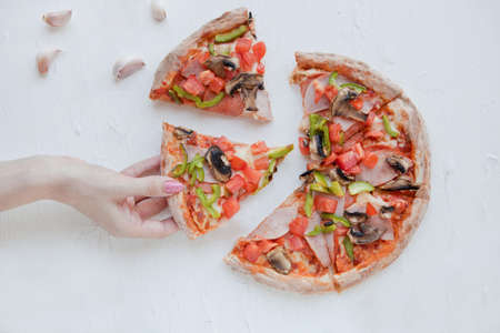 woman hand holding pizza slice with mushrooms, ham and garlic. sharing a delicious pizza on a white...