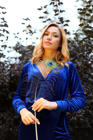 Beauty portrait of beautiful girl covering the face with peacock feather. Creative makeup peafowl feathers. Attractive mysterious lady. Bright harmonious colors, sari dress, shiny satin silk fabric.の写真素材
