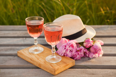 two glasses with rose wine and pink peony bouquet. delicious refreshing drink, huge blossoming flowers and mens hatの写真素材