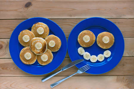 Pancakes with smile on blue plate and wooden background. banana fruit smiling breakfast - fun food for kidsの写真素材