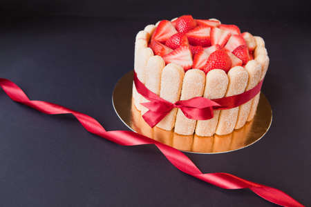 tiramisu cake with strawberries, ladyfingers, mascarpone and red bow-tape on black. charlotte cakeの写真素材