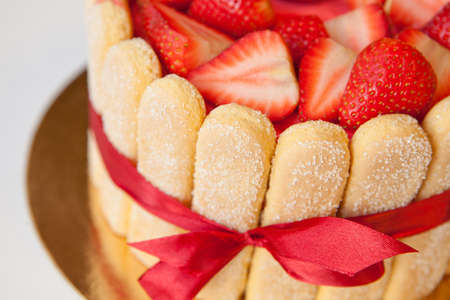 tiramisu cake close up with strawberries, ladyfingers, mascarpone and red bow-tape on whiteの写真素材