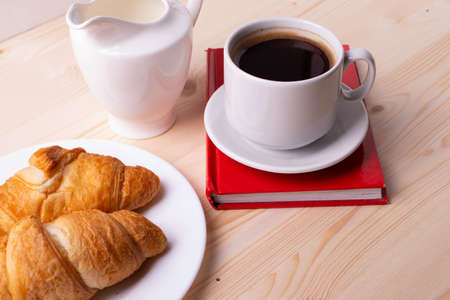 a white ceramic cup with black espresso, french croissant as breakfast or snack concept on rustic, natural texture wooden surfaceの写真素材