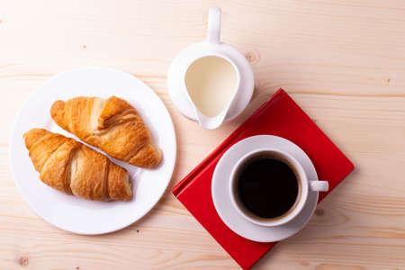 a white ceramic cup with black espresso, french croissant as breakfast or snack concept on rustic, natural texture wooden surfaceの写真素材