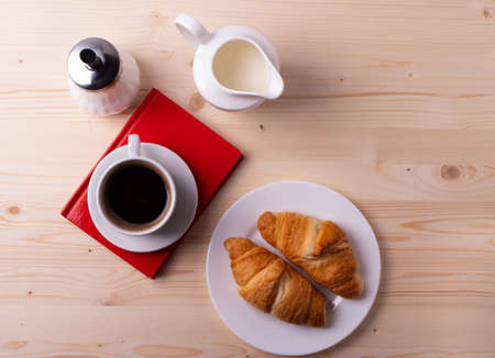 a white ceramic cup with black espresso, french croissant as breakfast or snack concept on rustic, natural texture wooden surfaceの写真素材