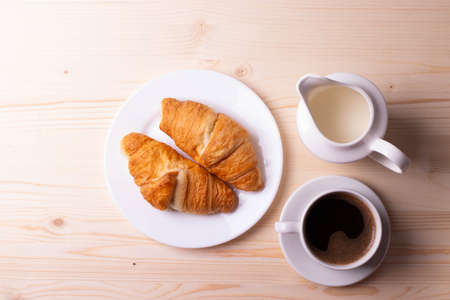 a white ceramic cup with black espresso, french croissant as breakfast or snack concept on rustic, natural texture wooden surfaceの写真素材