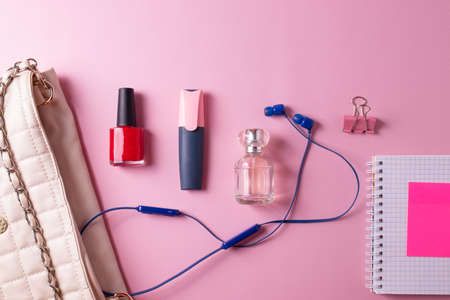 female beige clutch bag with different cosmetics and parfume containers and nail polishes on pink backgroundの写真素材